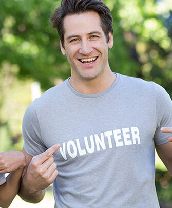 A man in grey shirt pointing to his volunteer t-shirt.